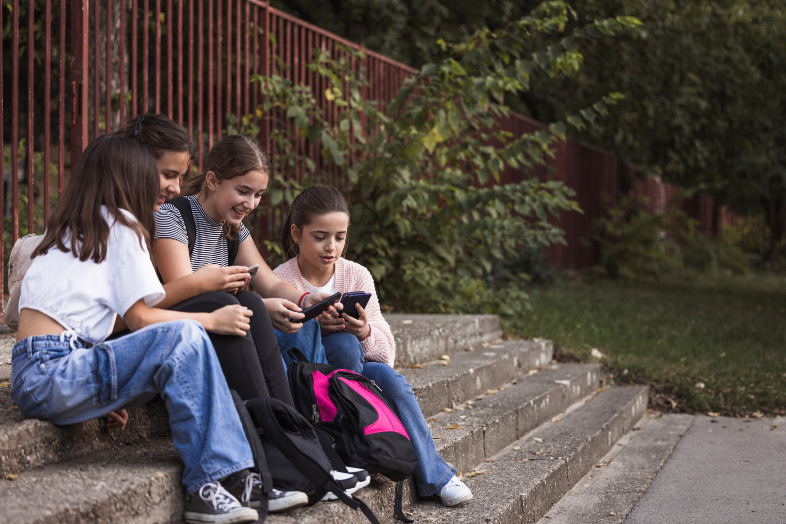 Happy school children resting on a staircase and playing games on their smart phones